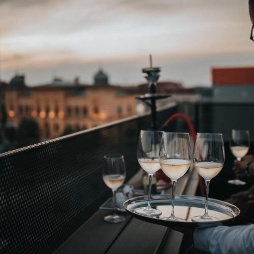 A waiter holding a tray with glasses of white wine on it and serving them to guests at the balcony